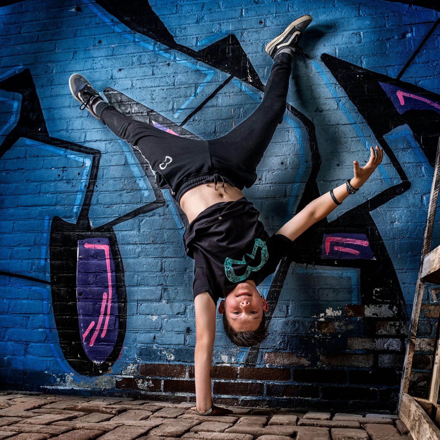 Breaker in handstand voor blauwe graffiti muur